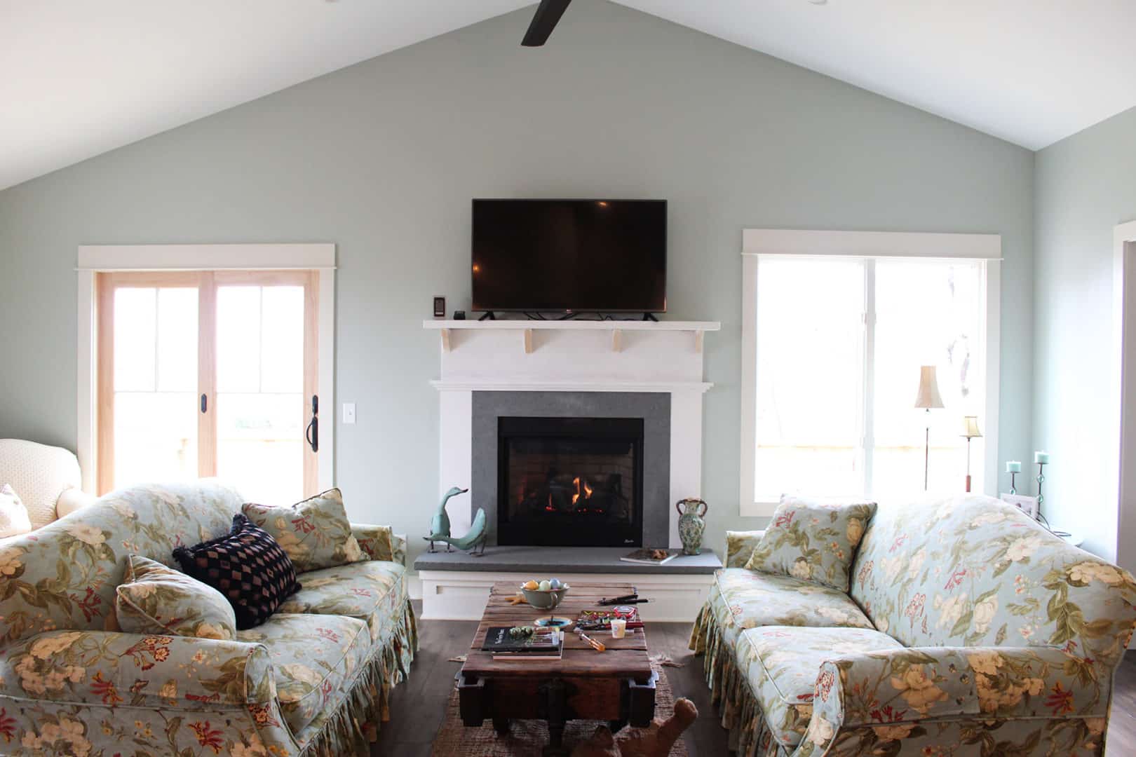 Living room with cozy fireplace, floral sofas, and large windows for natural light.