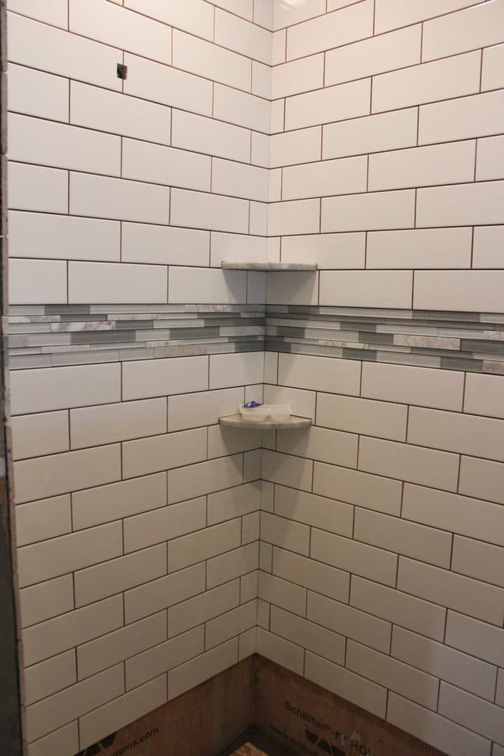 Modern tiled shower with white subway tiles and gray accent strip.