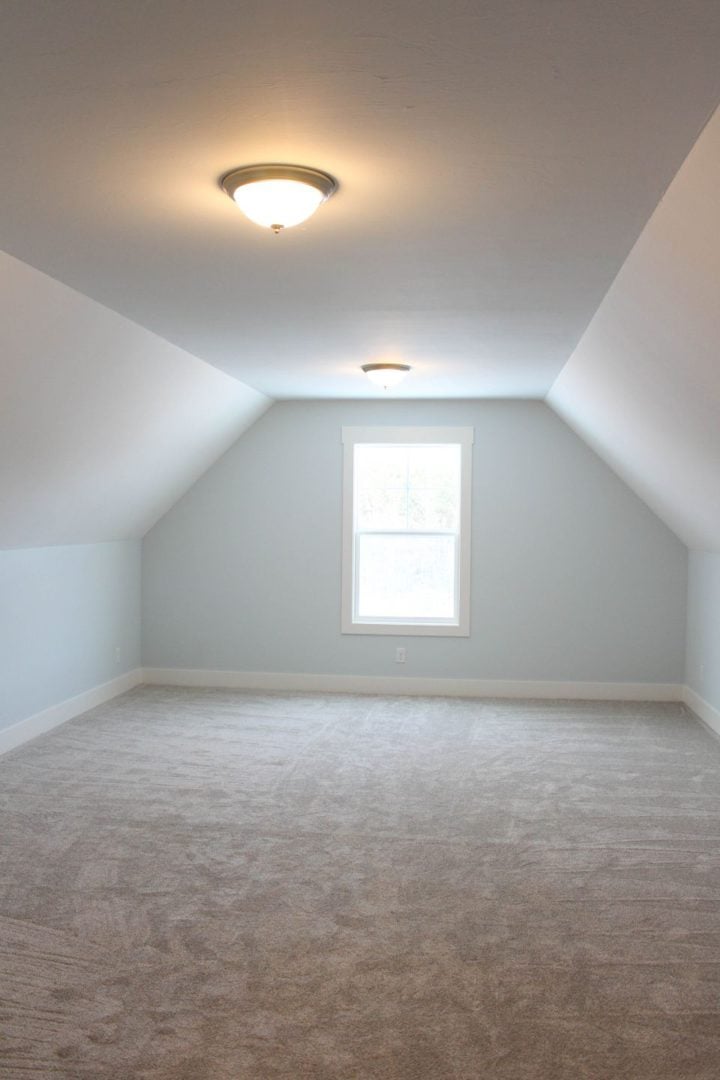 Bright attic bedroom with a large window and ceiling light fixture.