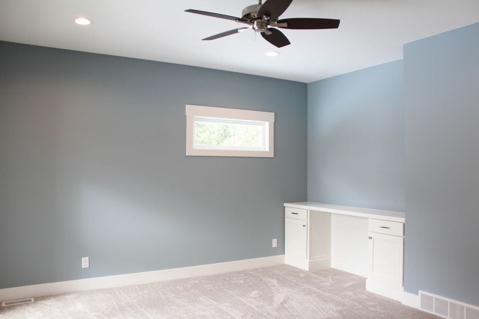 Modern bedroom with blue walls, white built-in desk, and ceiling fan.
