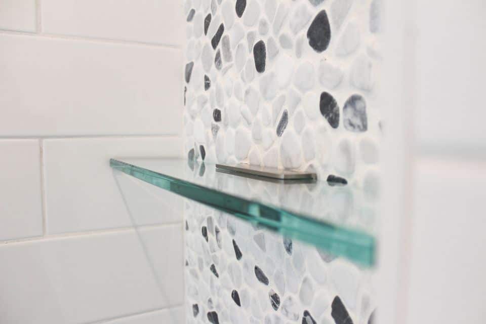 Shower wall with pebble tile and glass shelf in a modern bathroom.