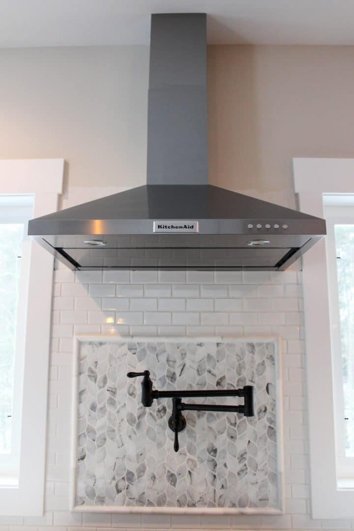 Modern stainless steel kitchen range hood with mosaic tile backsplash.