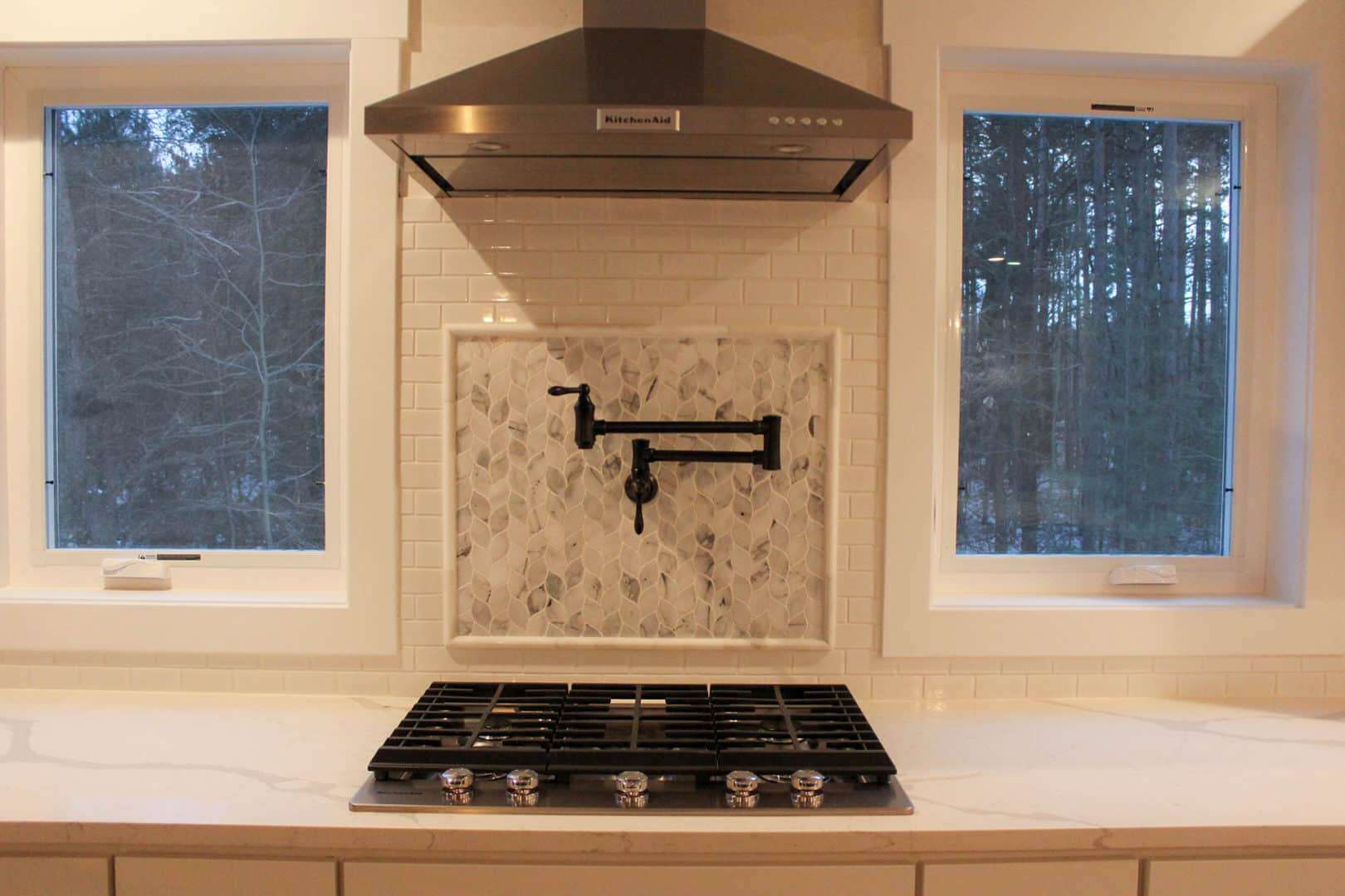 Modern kitchen stove with range hood and windows overlooking nature.