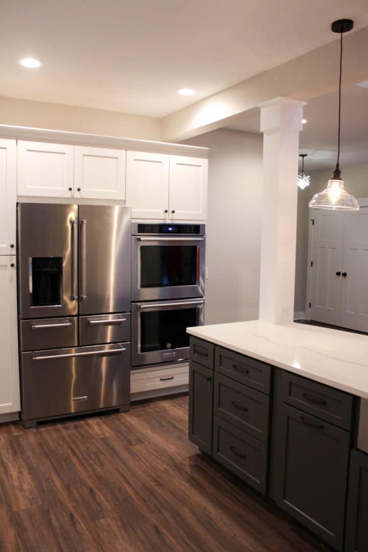 Modern kitchen with stainless steel refrigerator and double oven, white cabinets, and dark wood floo.