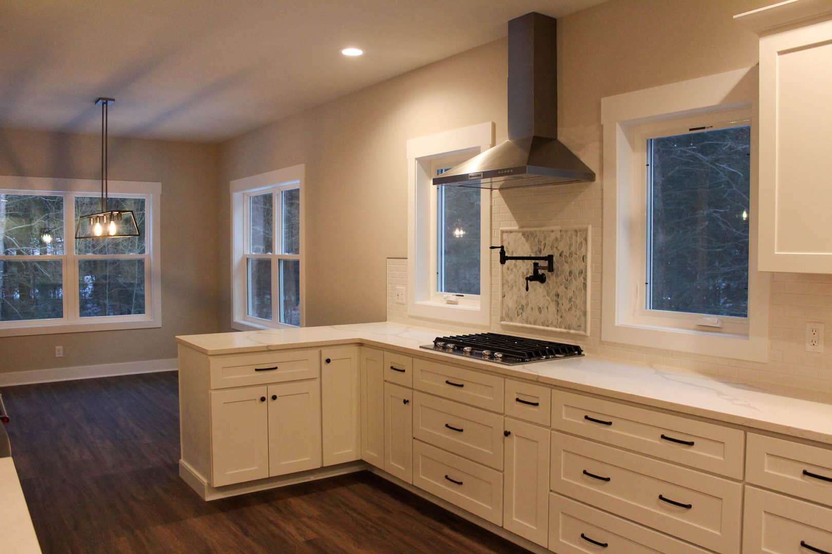 Modern kitchen featuring white cabinetry, a stainless steel range hood, and large windows for natura.
