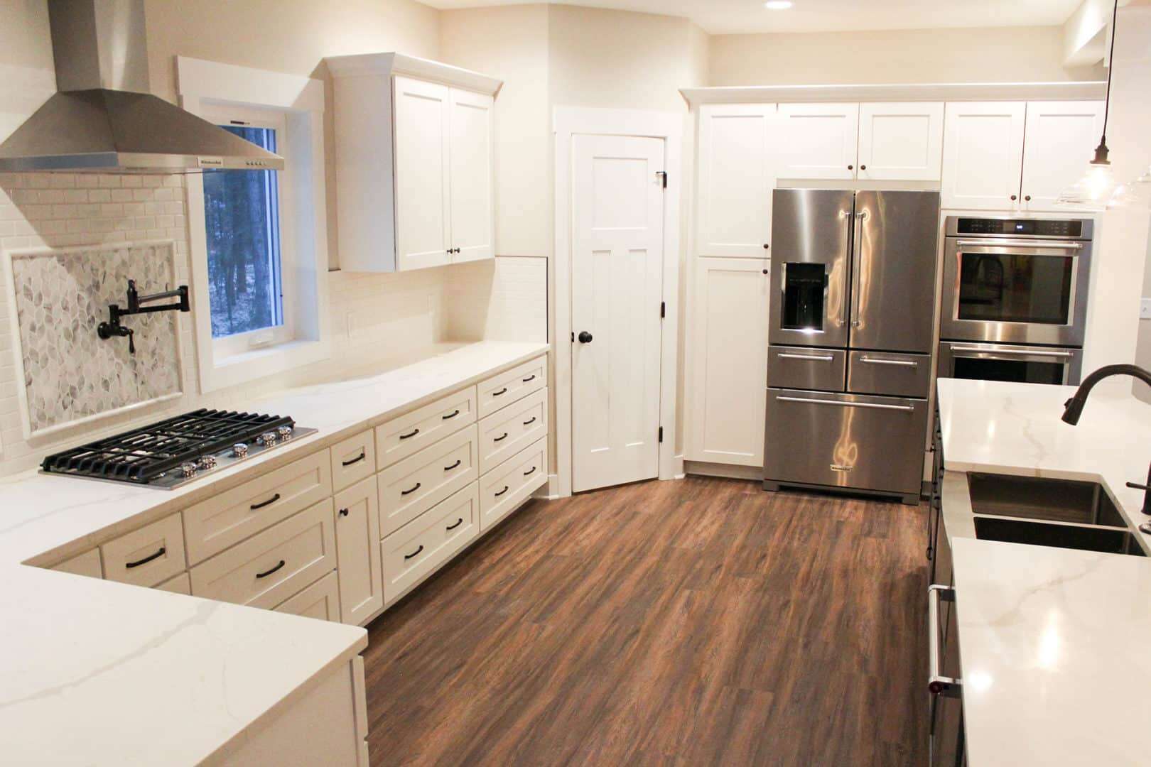 Bright white kitchen with stainless steel refrigerator, oven, and ample cabinet storage.