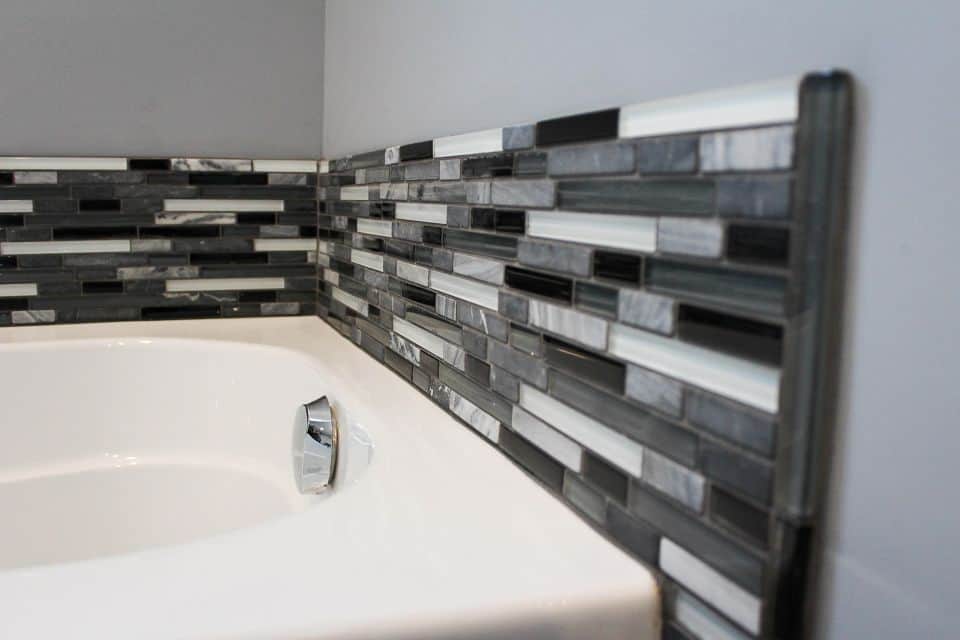 Modern bathroom with stylish black, gray, and white mosaic tile backsplash.
