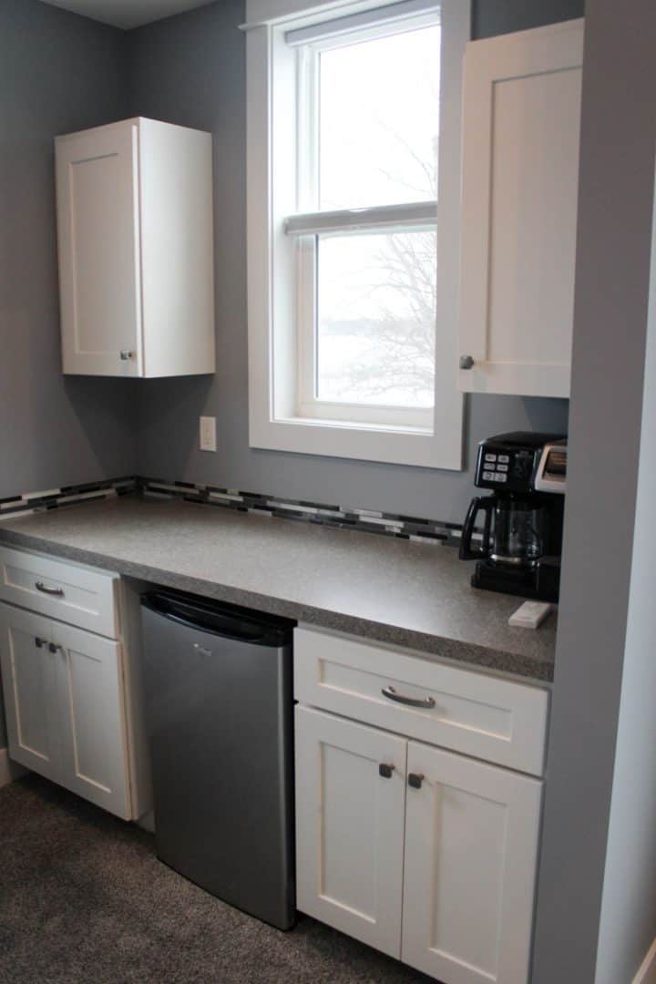 Bright kitchen featuring white cabinetry, gray countertop, and a coffee maker near a window.