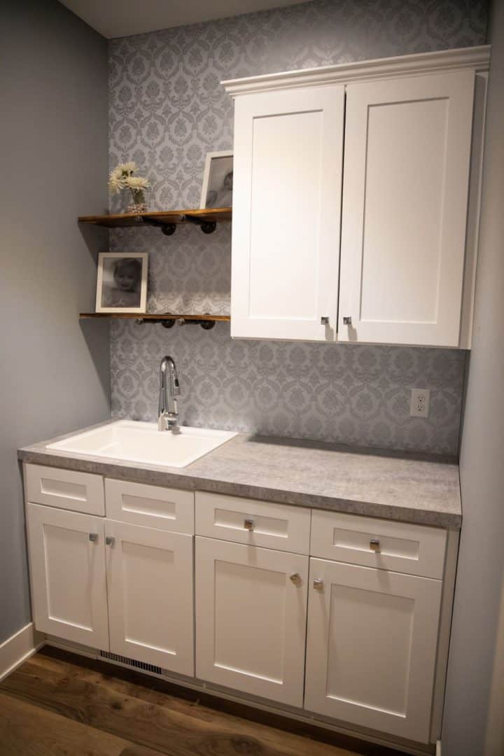 Modern kitchen sink and cabinetry with decorative wall shelves for storage and decor.