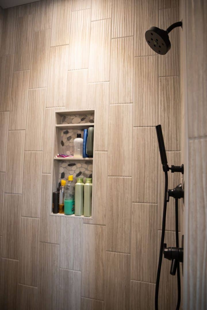 Modern tiled shower with built-in niche for toiletries and black shower fixtures.