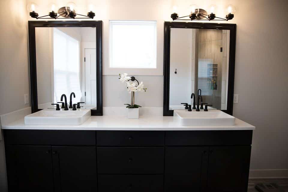 Double vanity bathroom with black cabinets, white sinks, and stylish lighting fixtures.
