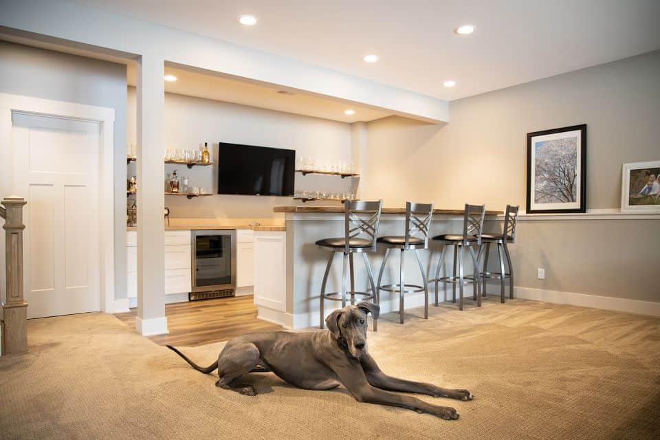 Modern basement bar with seating and a dog lying on the carpet.