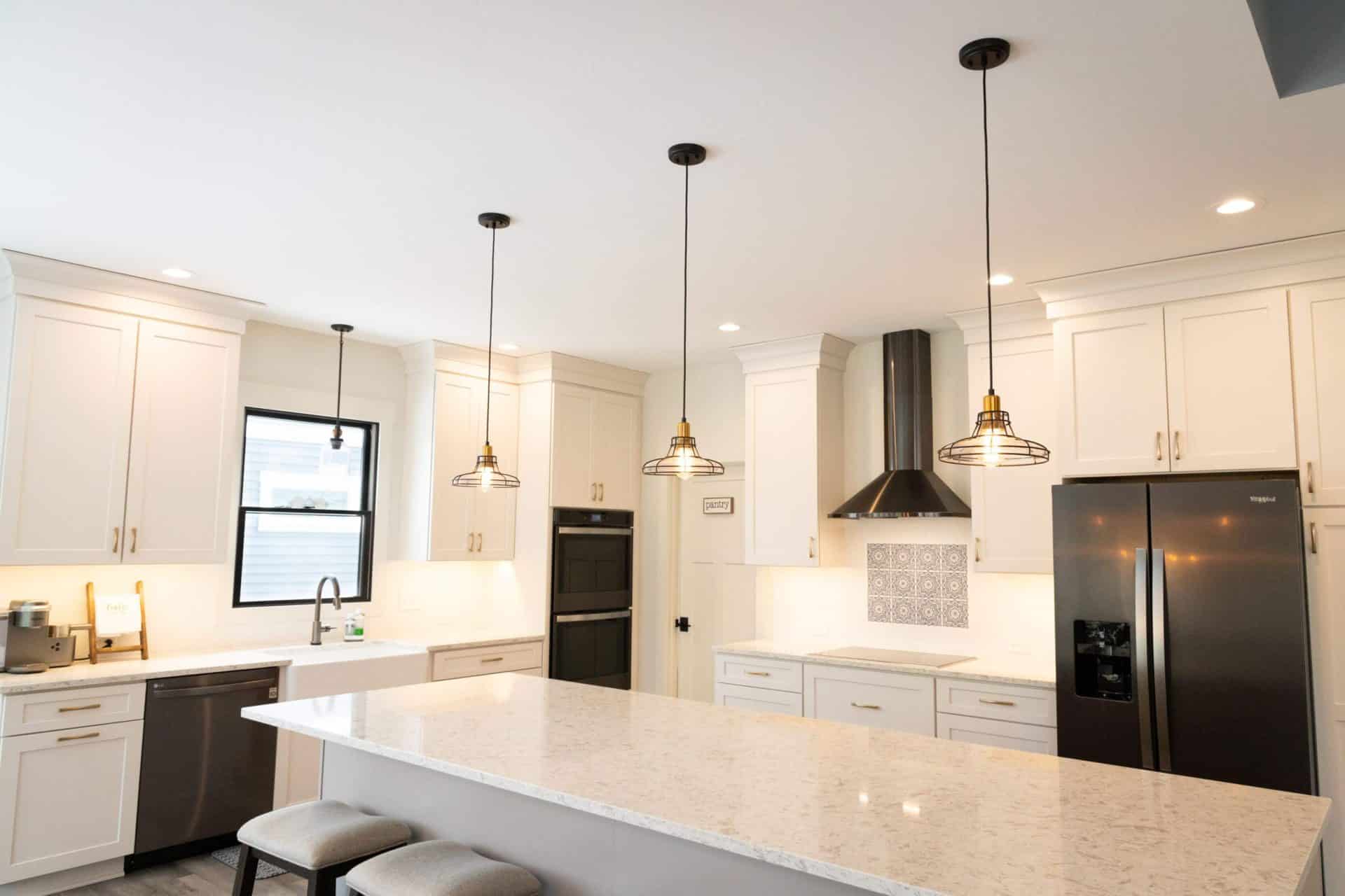Modern white kitchen with island, pendant lights, and stainless steel appliances.