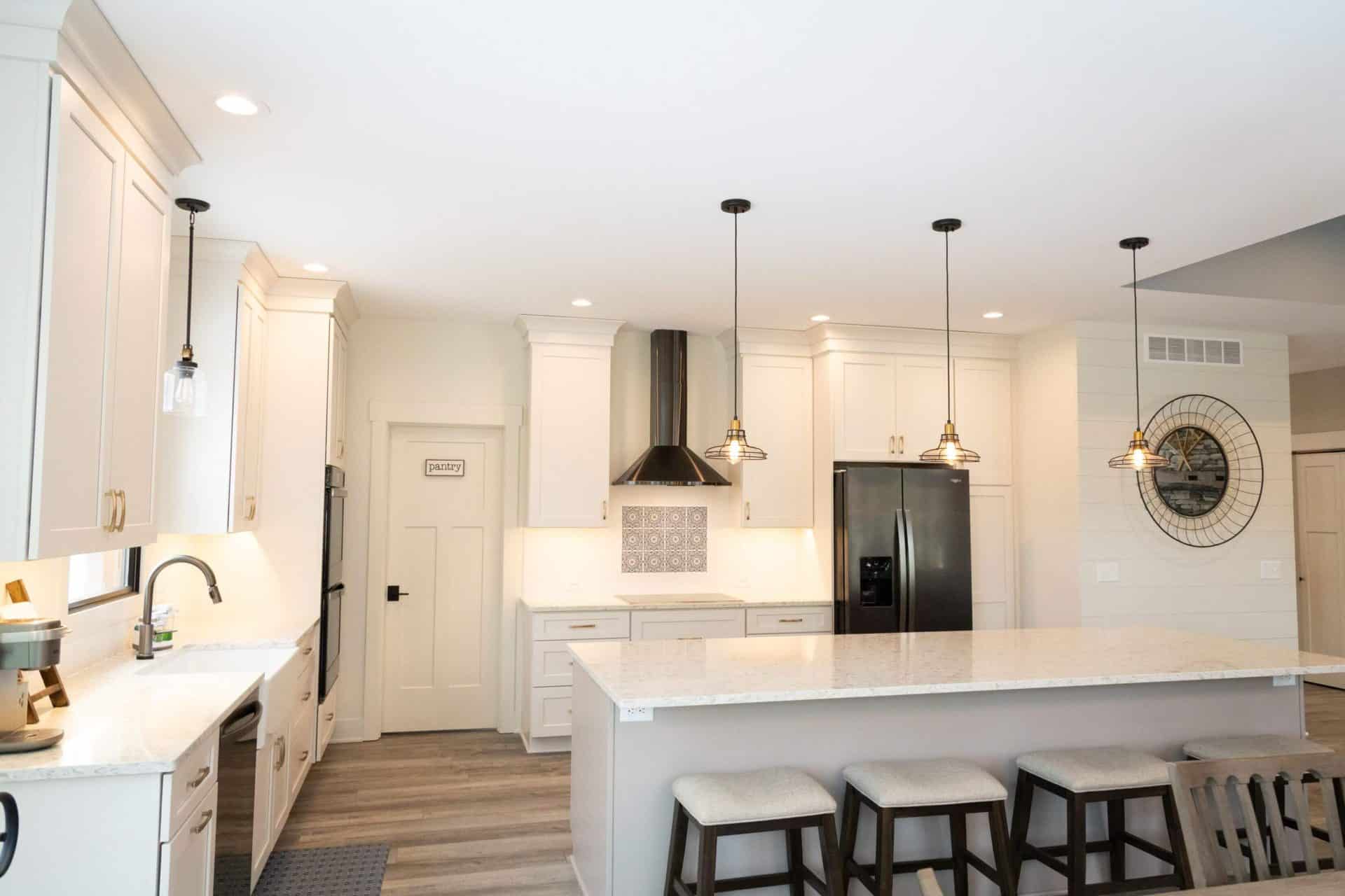 Modern white kitchen with island, pendant lights, and stainless steel appliances.