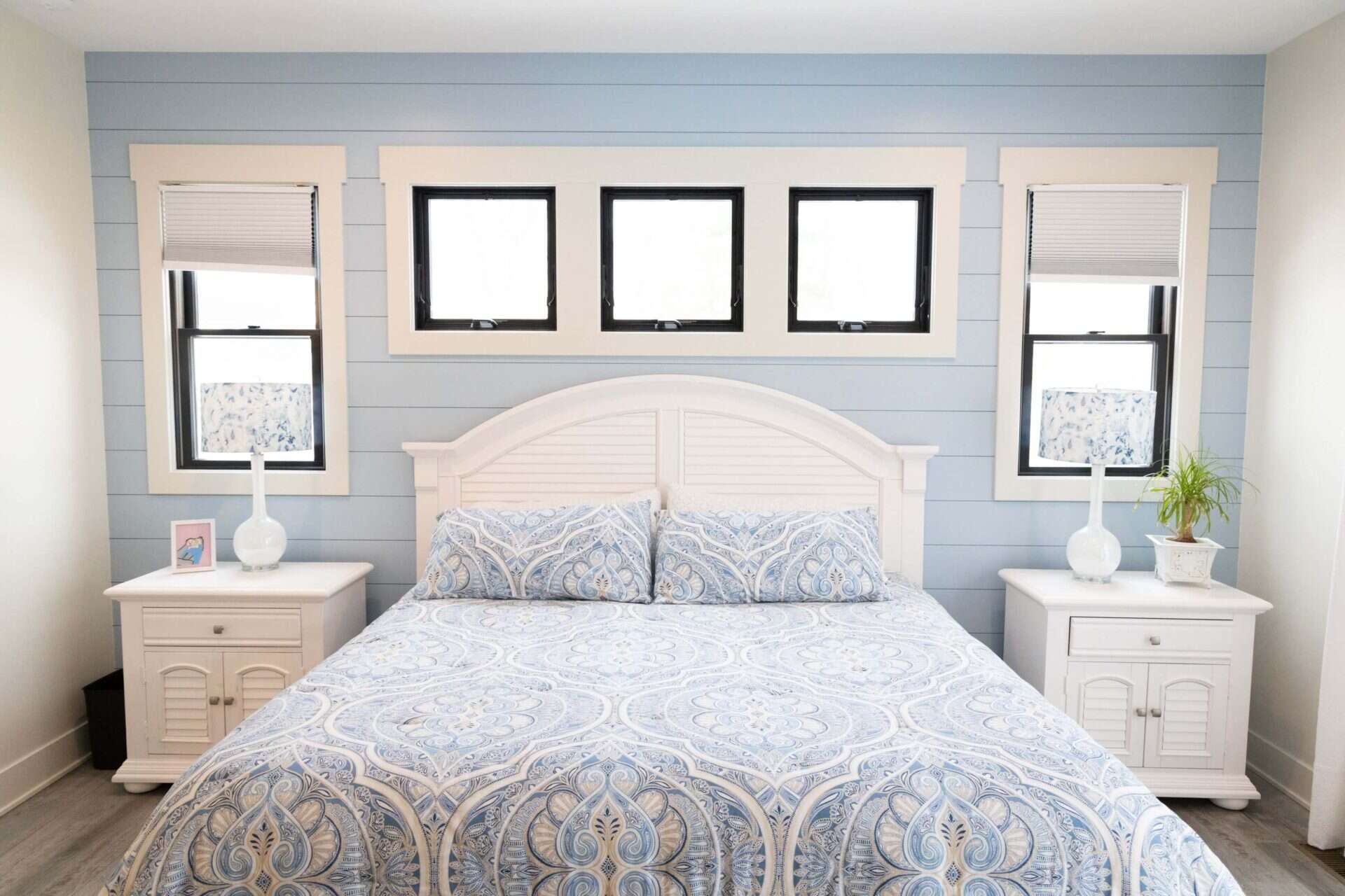 Bedroom with blue accent wall, white furniture, and large windows for natural light.