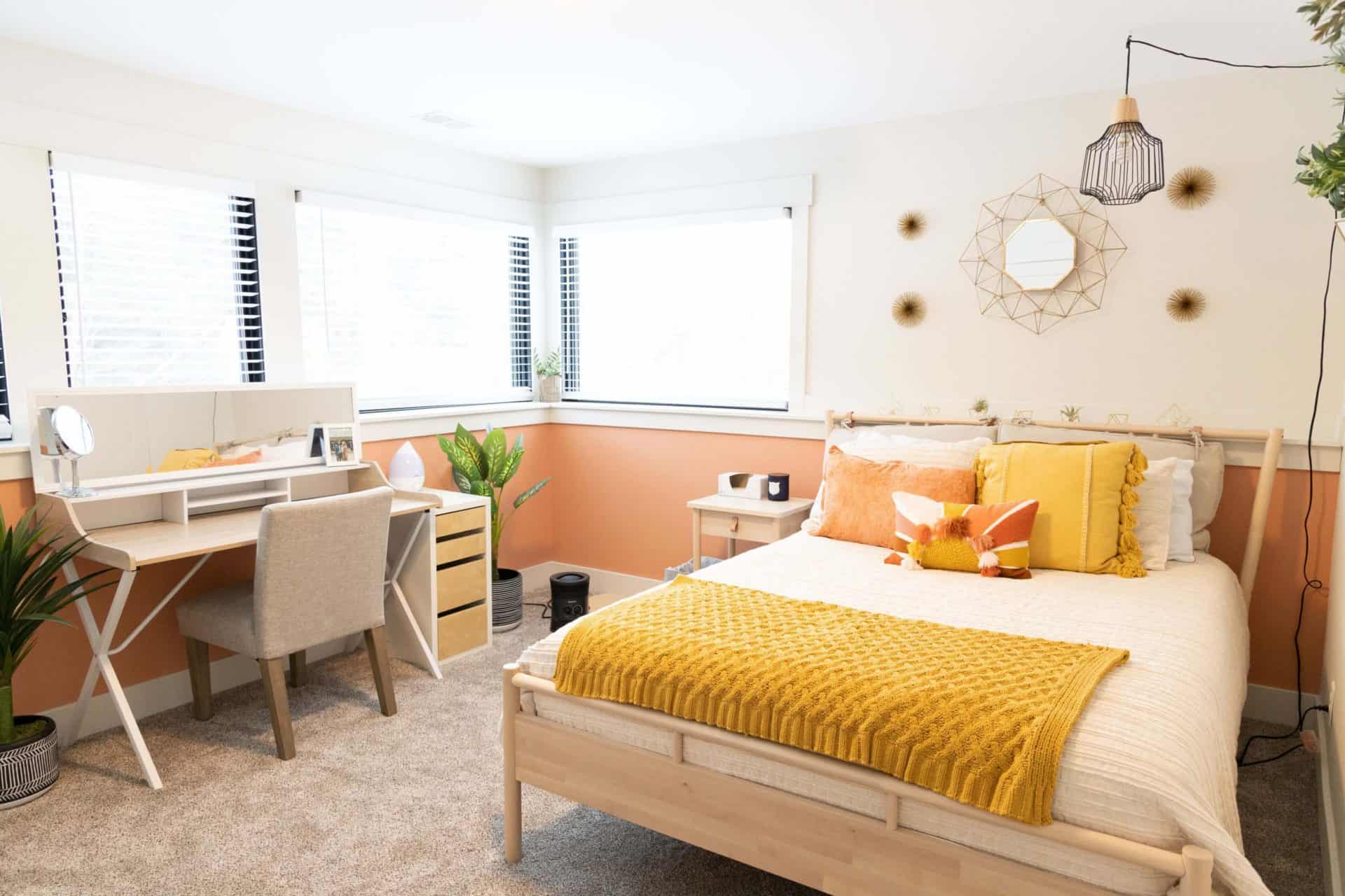 Bright bedroom with large windows, colorful pillows, and stylish wall decor.