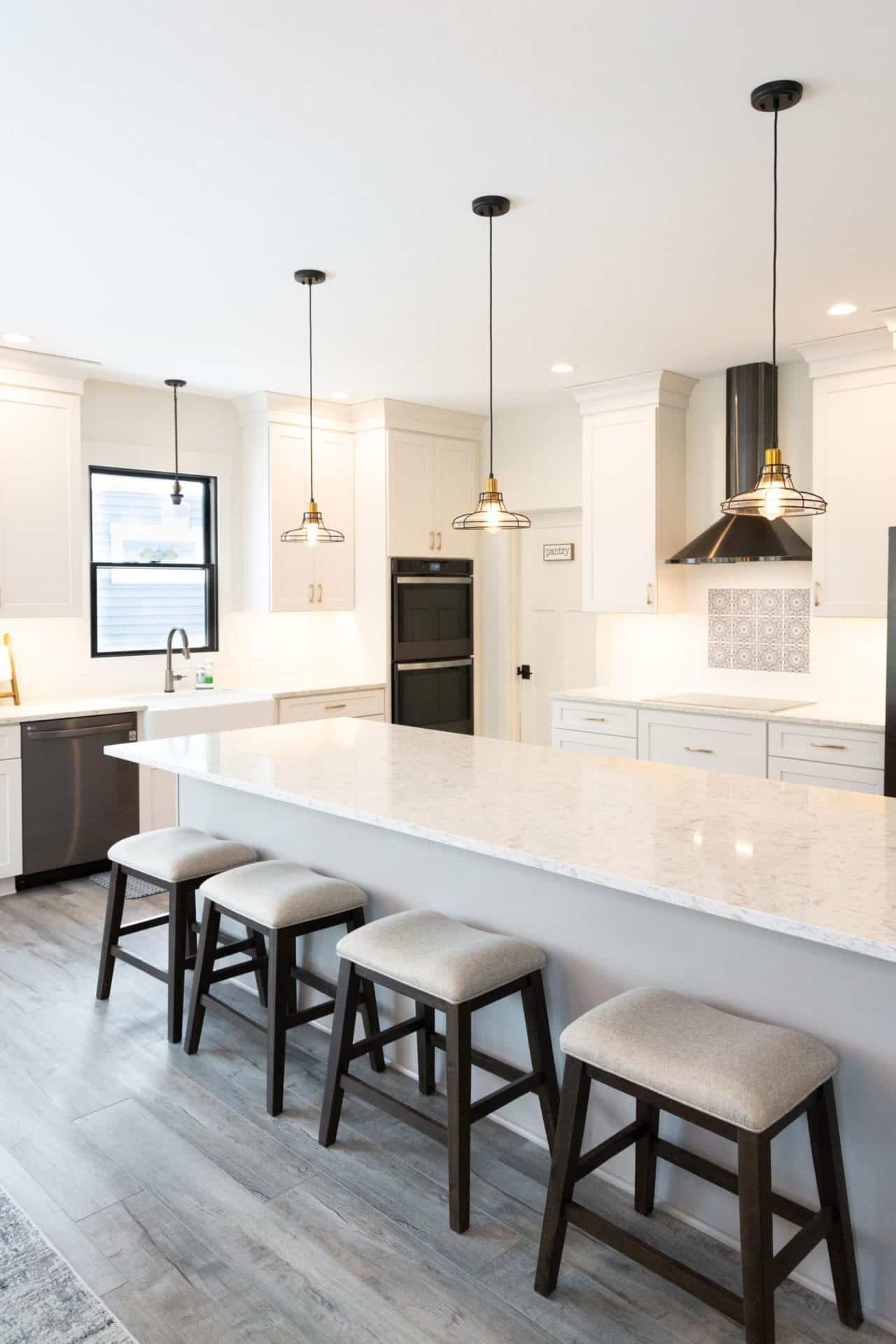Bright, modern kitchen featuring a large island, white cabinetry, and black pendant lights for a sty.