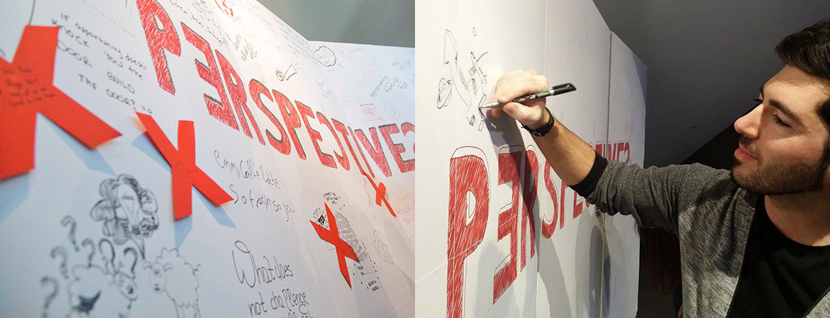 A young man drawing and writing on a large whiteboard with red and black markers.