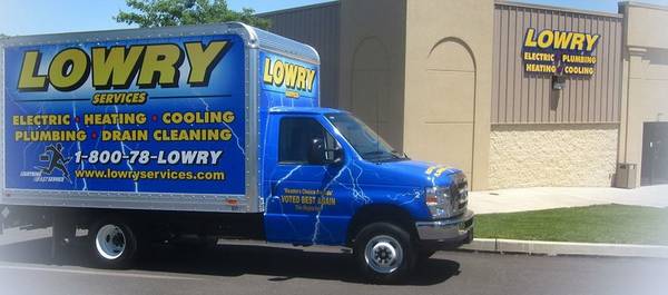A blue Lowry Services truck is parked outside a Lowry Services building, advertising electric, plumbing, heating, cooling, and drain cleaning services—just some of what earns them positive customer reviews.