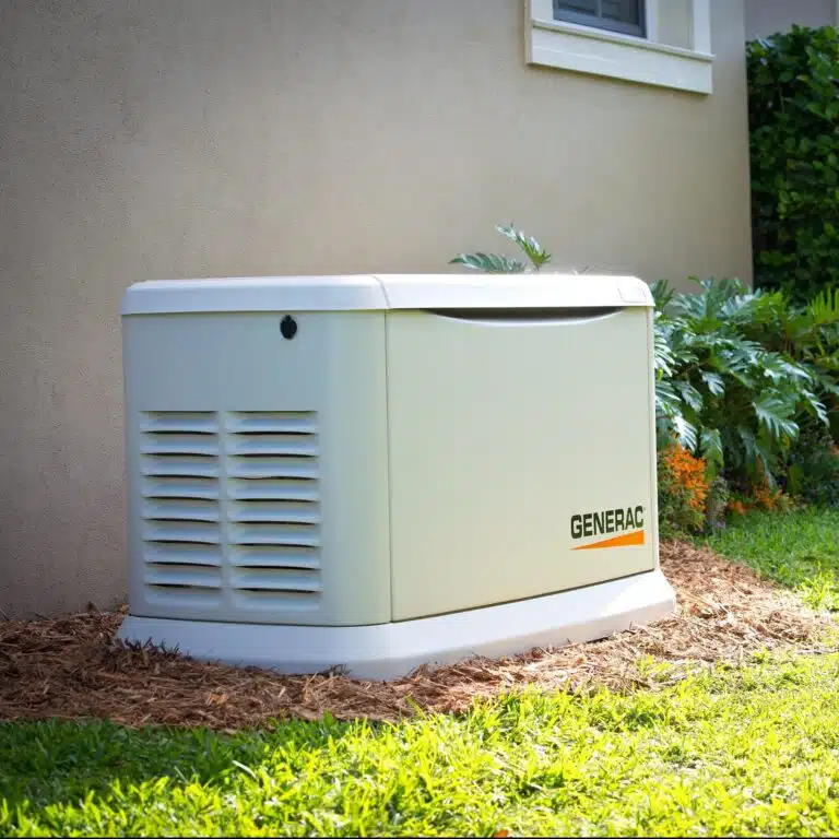 A Generac standby generator is installed outside a house near a window, surrounded by mulch, plants, and grass.