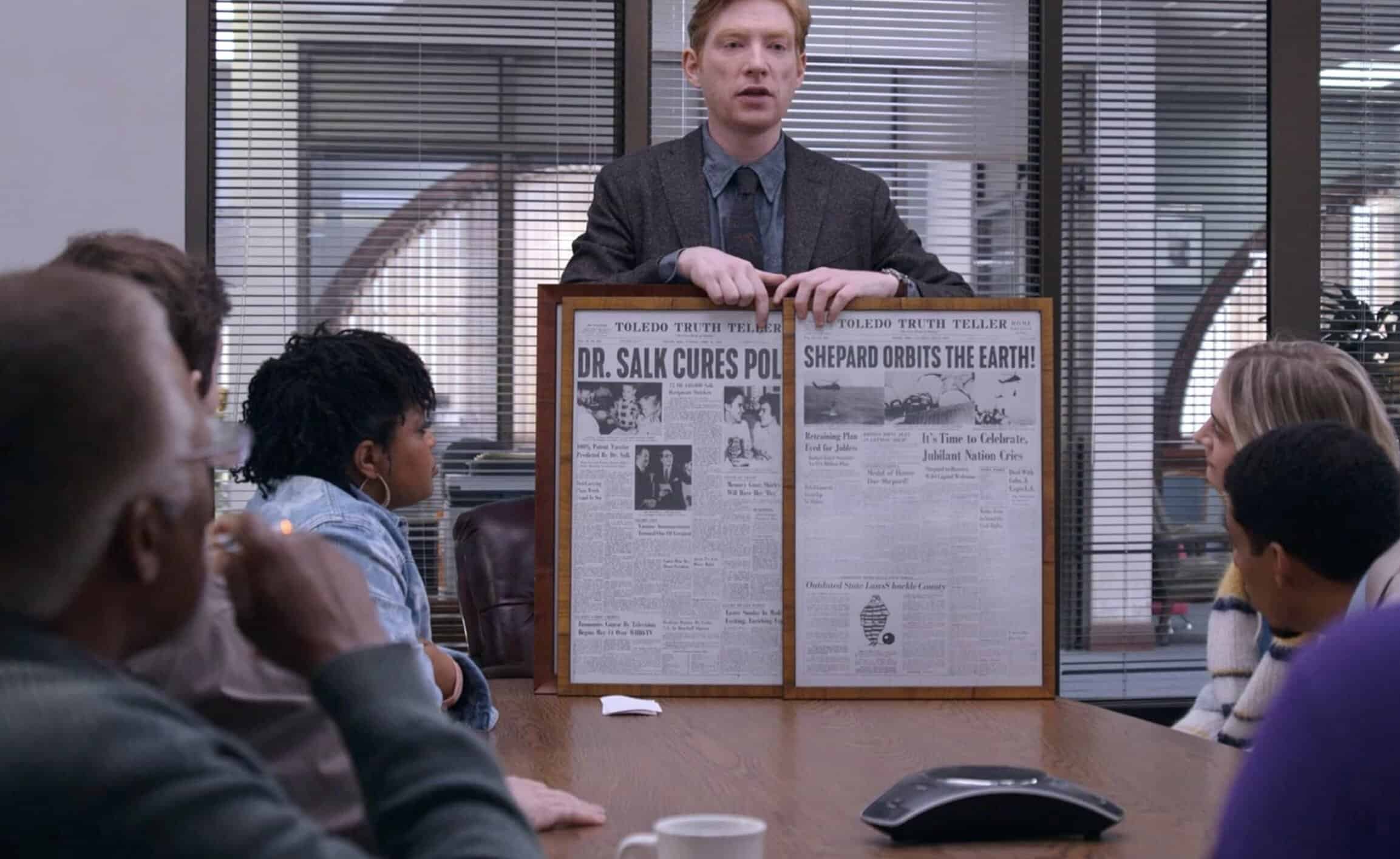 Elevstående person håller upp ett stort nyhetsplakat i ett mötesrum, omgivet av engagerade åhörare i ett professionellt kontorsmiljö.