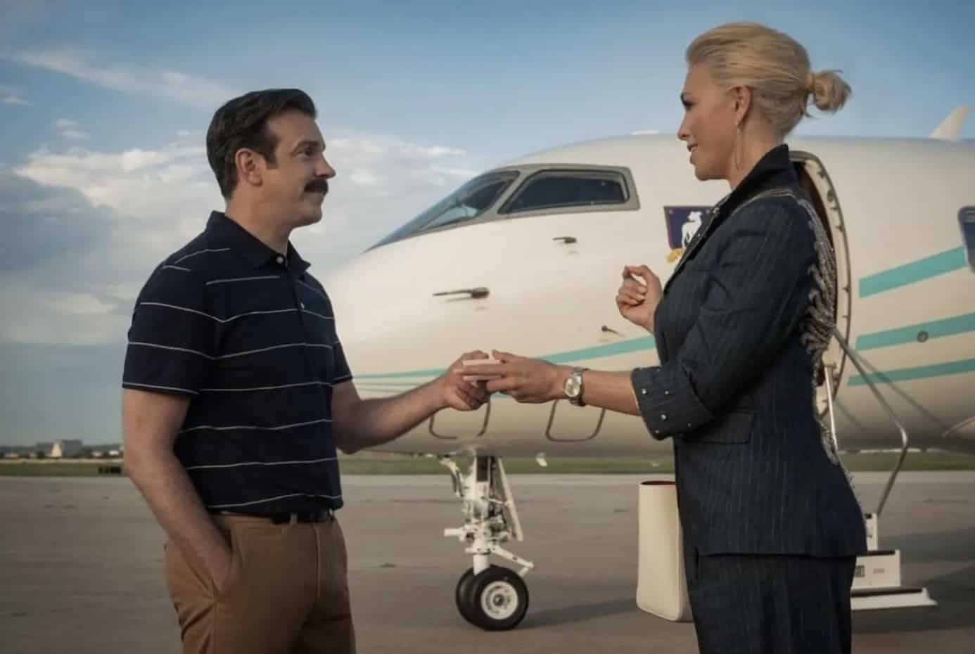 - En man och en kvinna står utanför ett privatflygplan på en flygplats, symboliserar exklusivitet och lyx.