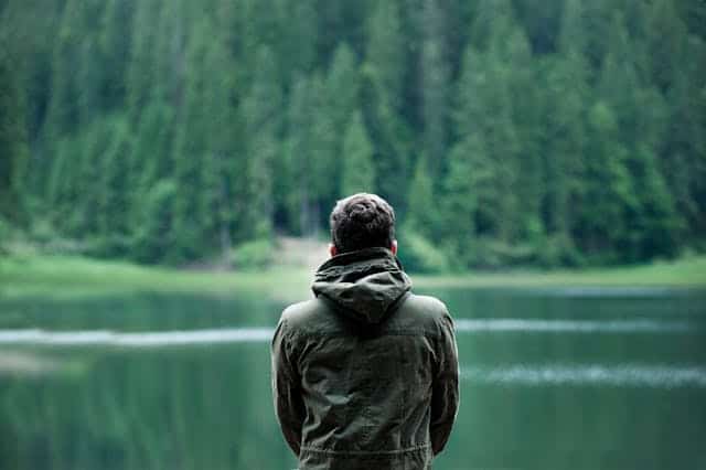Persona davanti a un lago e foresta; quando un uomo non ti ama, ti dà le spalle