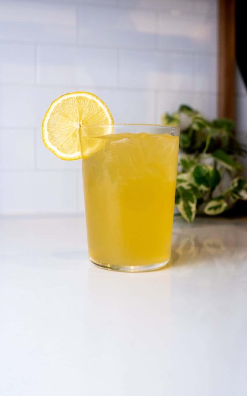 Refreshing glass of lemonade with lemon slice on a white countertop.