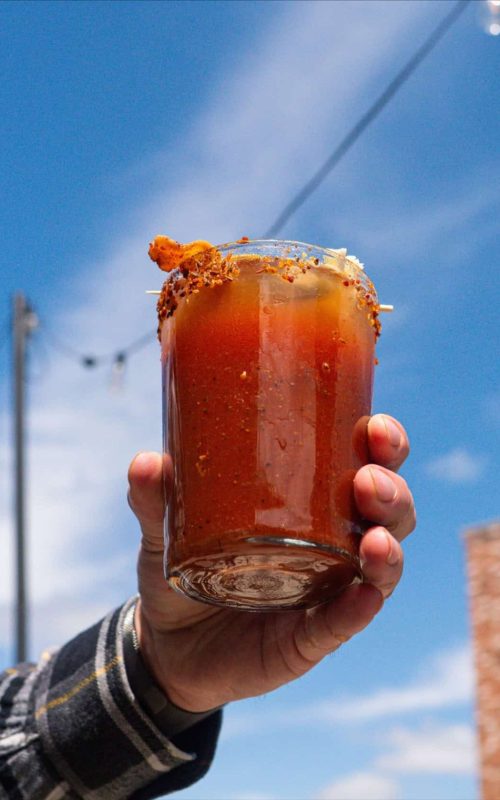 Spicy cocktail with a salted rim held up against a blue sky background.