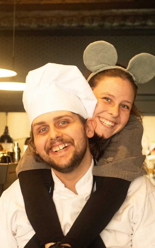 Chef and girl with mouse ears, smiling in a restaurant setting.