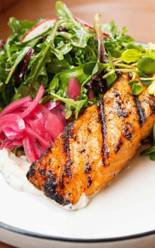 Healthy grilled salmon served with a vibrant mixed green salad and tangy pickled vegetables. Perfect.