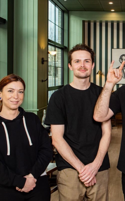 Team of three staff members smiling inside Mudpenny restaurant.