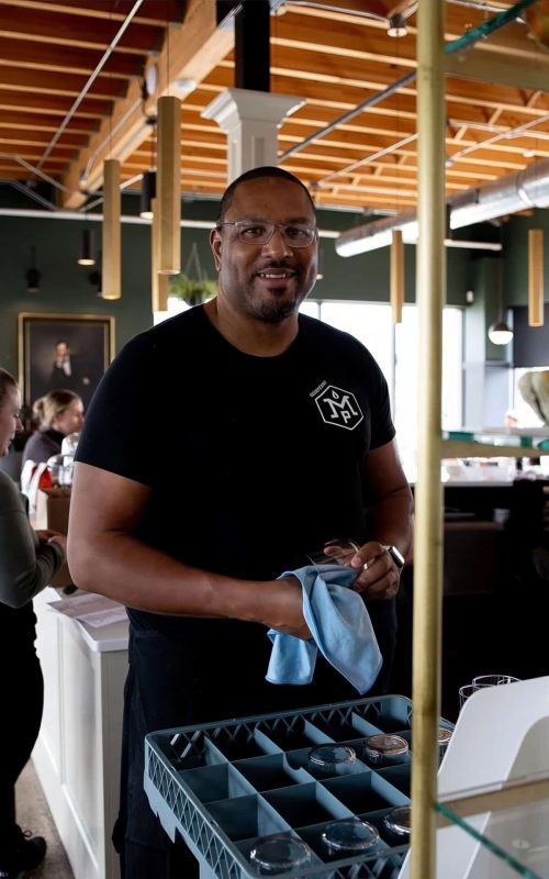 Smiling staff member holding a cloth in a modern restaurant setting.