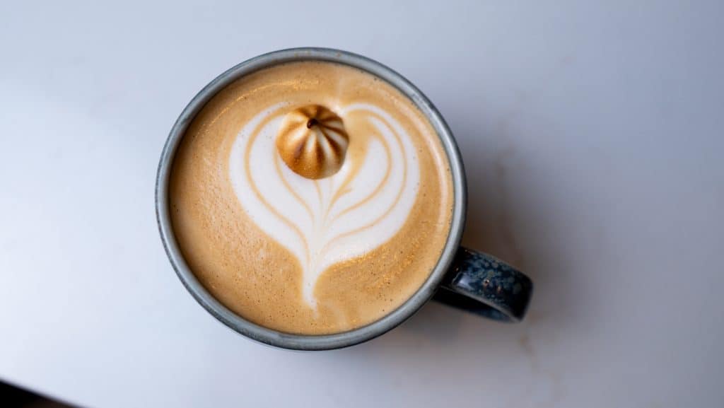 Coffee latte with latte art heart design in a black mug on a white surface.
