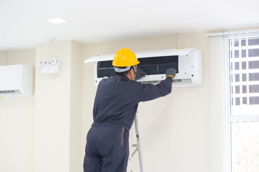EFFICIENT HVAC TECHNICIAN SERVICING WALL-MOUNTED AIR CONDITIONER IN MODERN HOME FOR OPTIMAL COOLING.