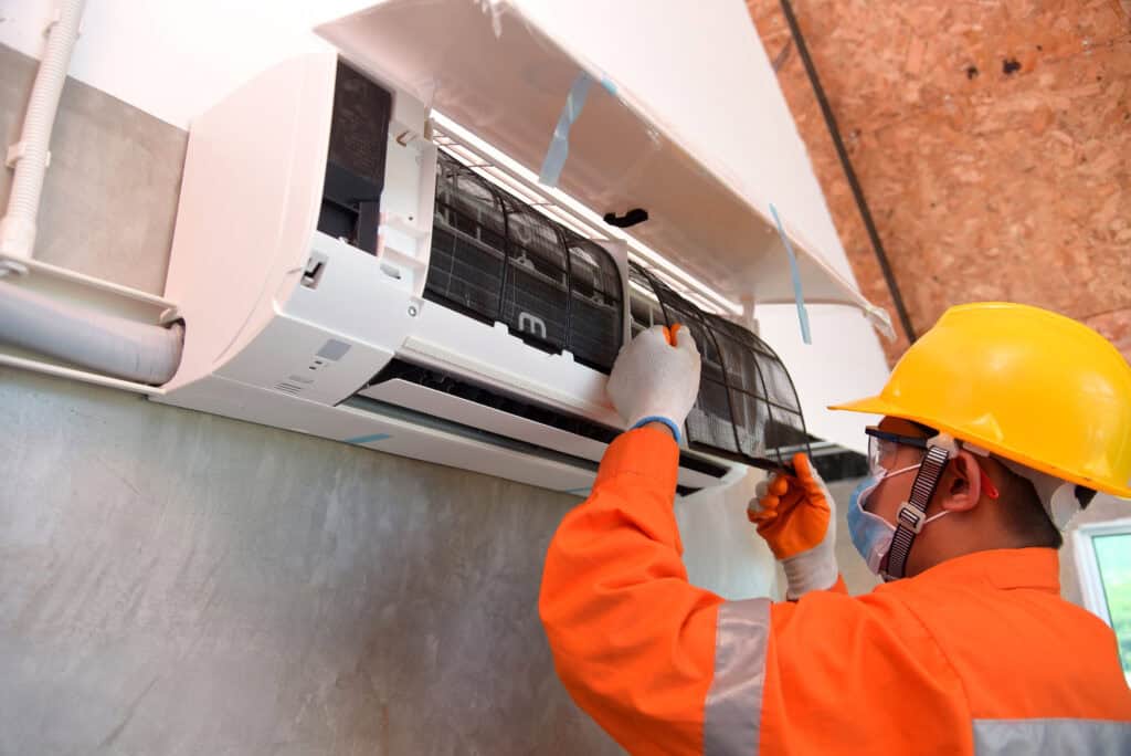 EFFICIENT HVAC TECHNICIAN SERVICING WALL-MOUNTED AIR CONDITIONER, EMPHASIZING TOP-RATED HVAC AND PLUMBING SERVICES.