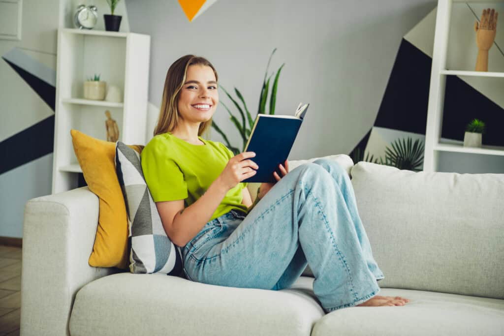 CLEAN, MODERN LIVING ROOM FEATURING YOUNG WOMAN RELAXING ON A SOFA, READING A BOOK, WITH STYLISH DECOR, PERFECT FOR HIGHLIGHTING COMFORTABLE HOME ENVIRONMENT AND HVAC OR PLUMBING SERVICES.