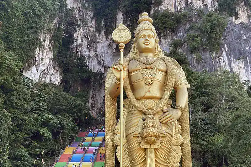 The Ultimate Guide To The 10 Best Day Trips from Kuala Lumpur (Local Expert Edition) 10 The golden Lord Murugan statue at Batu Caves with the colourful staircase and limestone cliffs behind it.