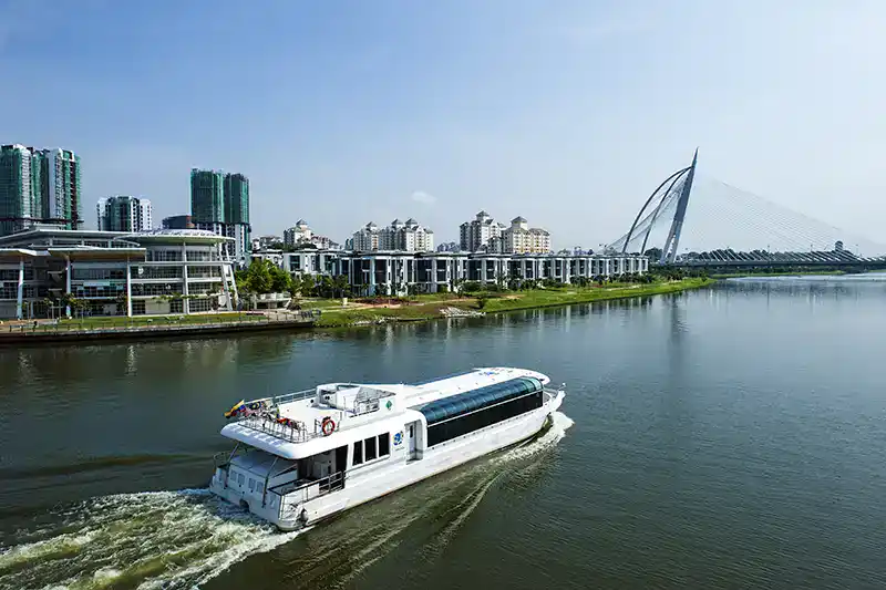 The Ultimate Guide To The 10 Best Day Trips from Kuala Lumpur (Local Expert Edition) 6 A sightseeing boat cruising along the lake in Putrajaya with modern buildings and a cable-stayed bridge in the background.