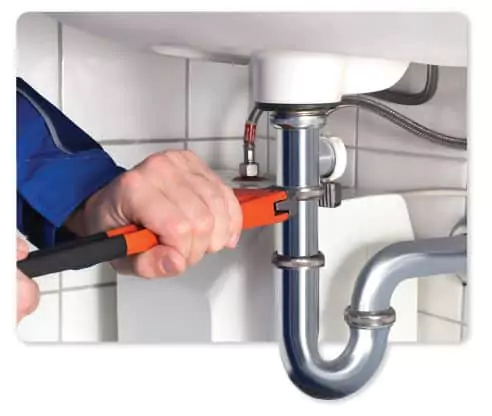 A person uses a pipe wrench to tighten or loosen the plumbing under a sink, ensuring secure contact between the pipes and fittings.
