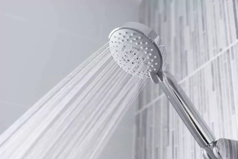 A close-up of a chrome showerhead spraying water in a tiled bathroom, capturing every droplet as it makes contact with the surface.