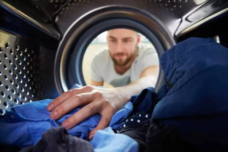 View from inside a washing machine as a person loads laundry, reaching in with one hand to place clothes into the drum, making contact with the soft fabric.