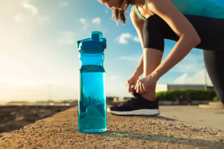 A close-up of a blue water bottle on a ledge, with a person in athletic wear tying their shoelaces outdoors—ready for action and contact with the day ahead.