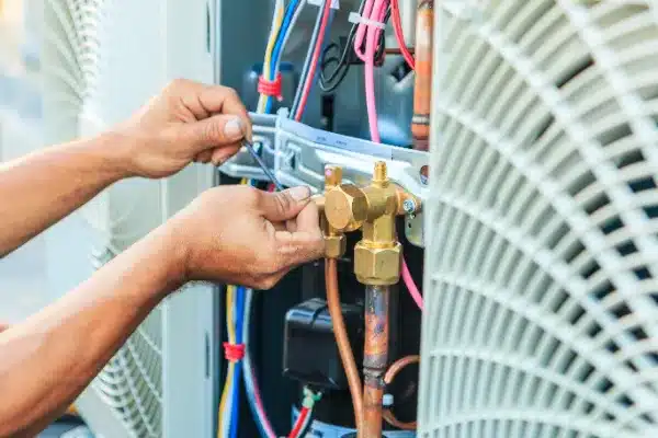 A person uses a wrench to adjust components and wires inside an HVAC unit during air conditioning maintenance, with various cables and pipes visible in Fairfax, VA.