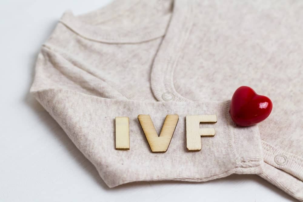 IVF letters with a red heart on a beige baby onesie for fertility treatment.