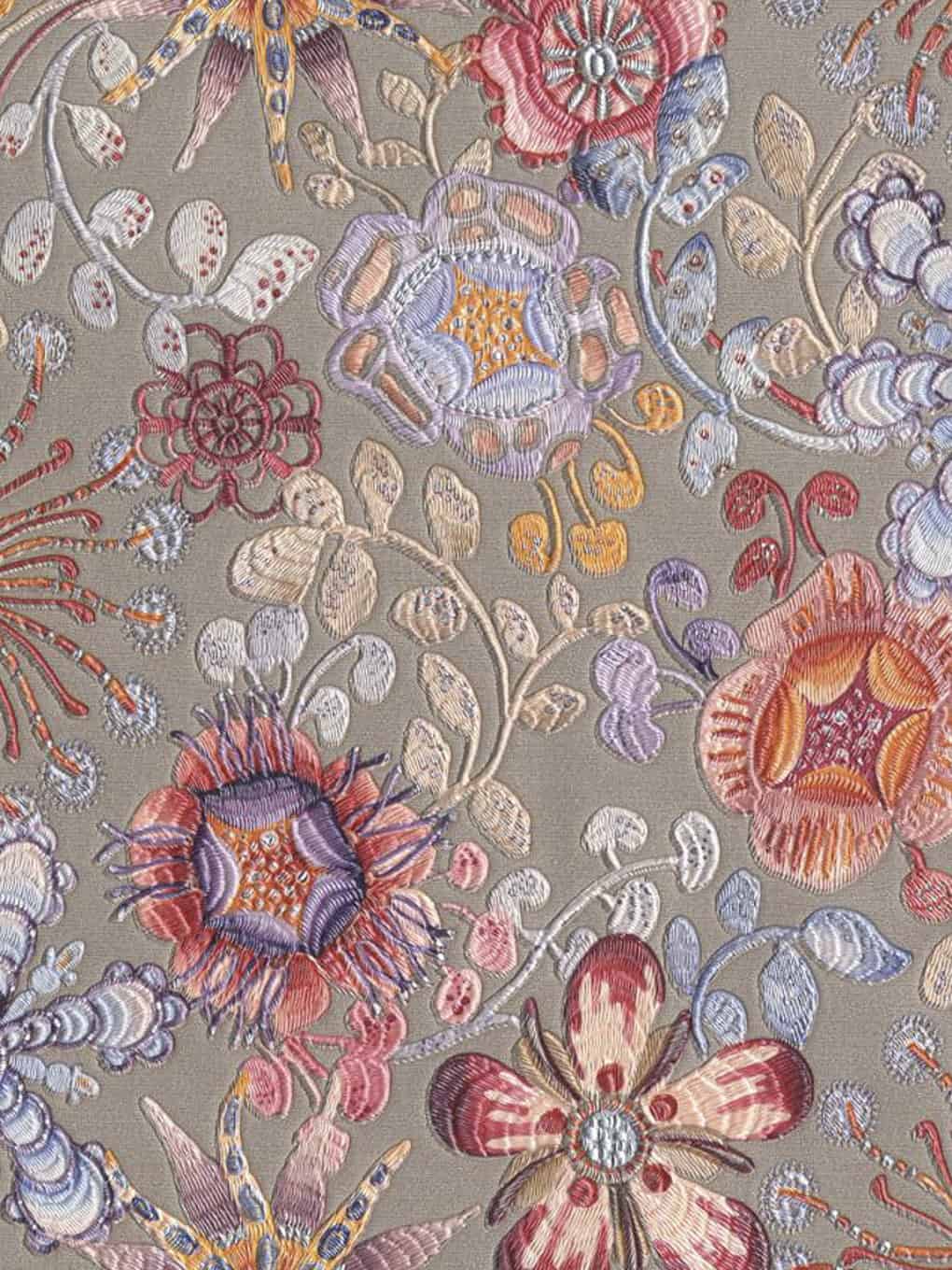 Embroidered floral textile featuring detailed flowers and leaves in pastel shades on a neutral backg.