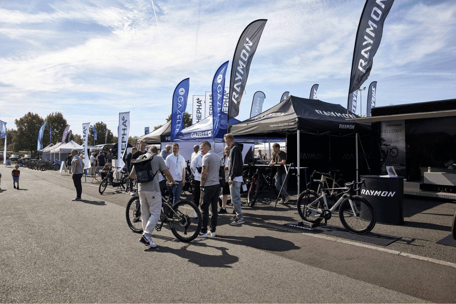 Menschen auf einer Fahrradmesse mit Raymon- und Canyon-Flaggen im Hintergrund.