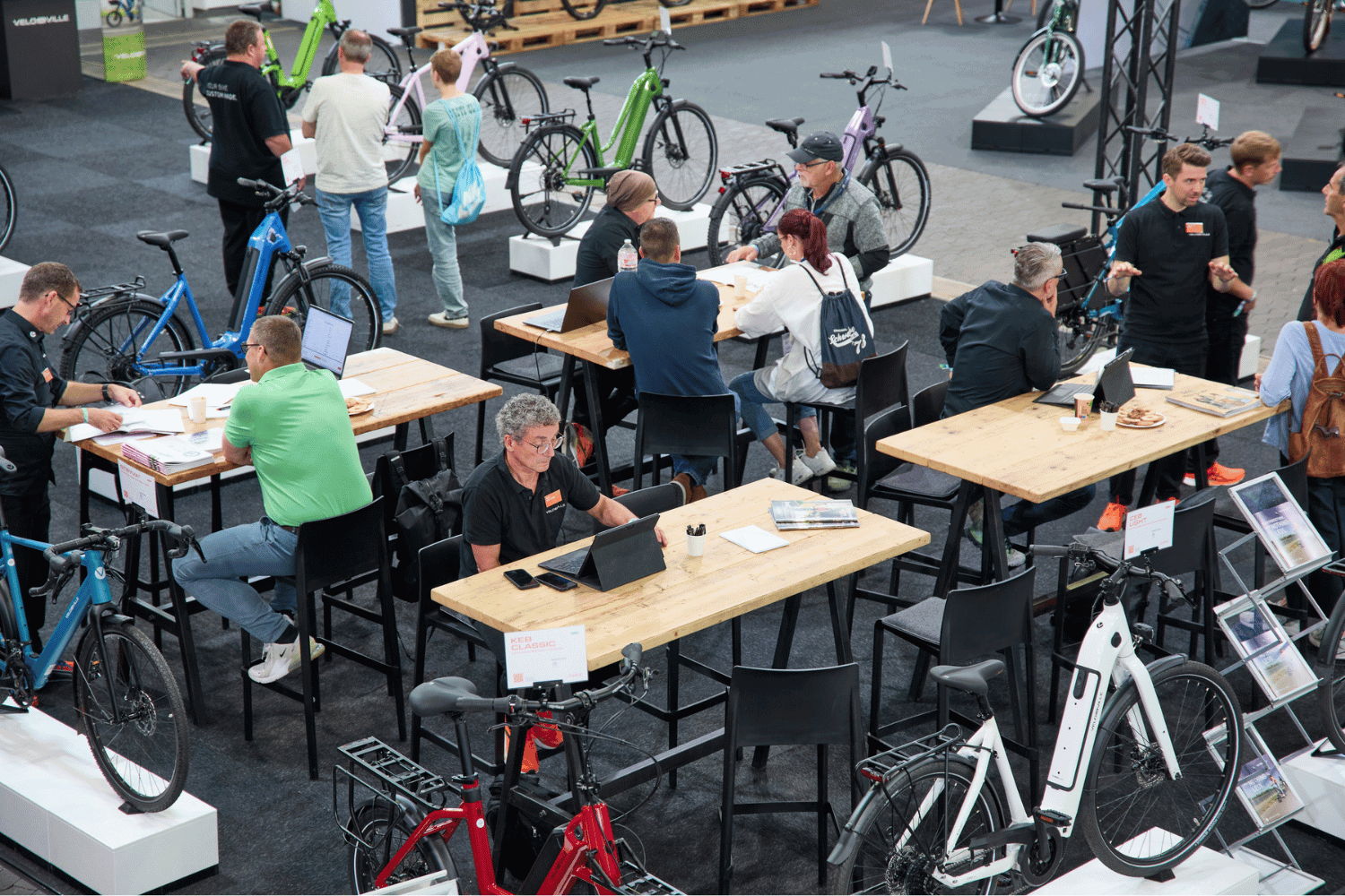 Menschen auf einer Fahrradmesse mit verschiedenen E-Bikes und Fahrradzubehör.