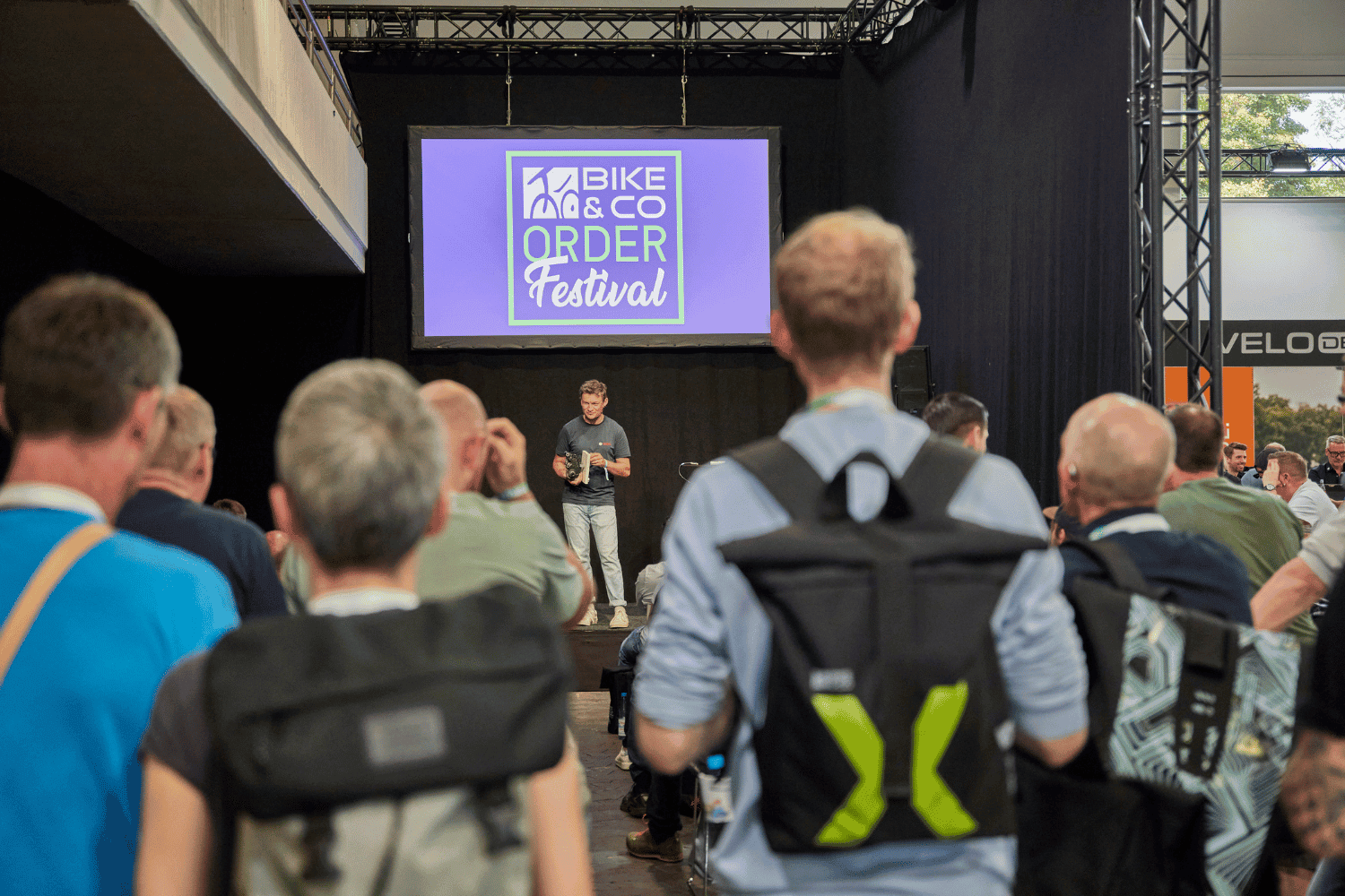 Teilnehmer beim Bike & Co Order Festival mit Präsentation auf Bühne.