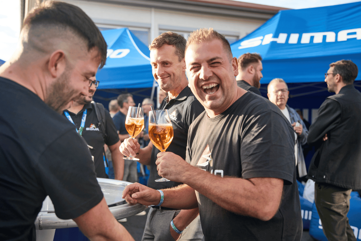 Freunde feiern bei einem Event mit Getränken und Zelt im Hintergrund.